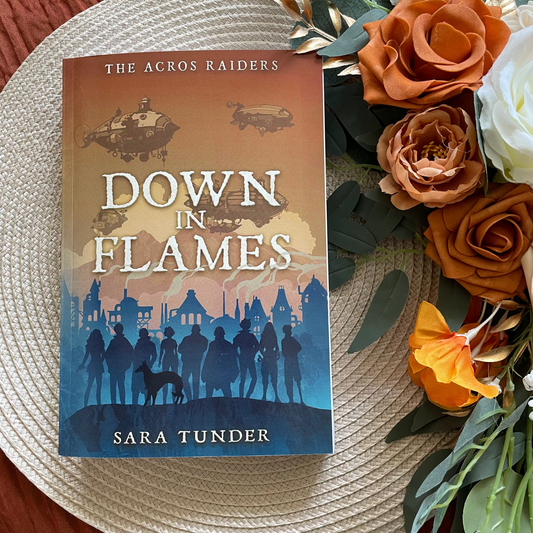 Book titled 'Down in Flames' by Sara Tunder on a woven surface with flowers.